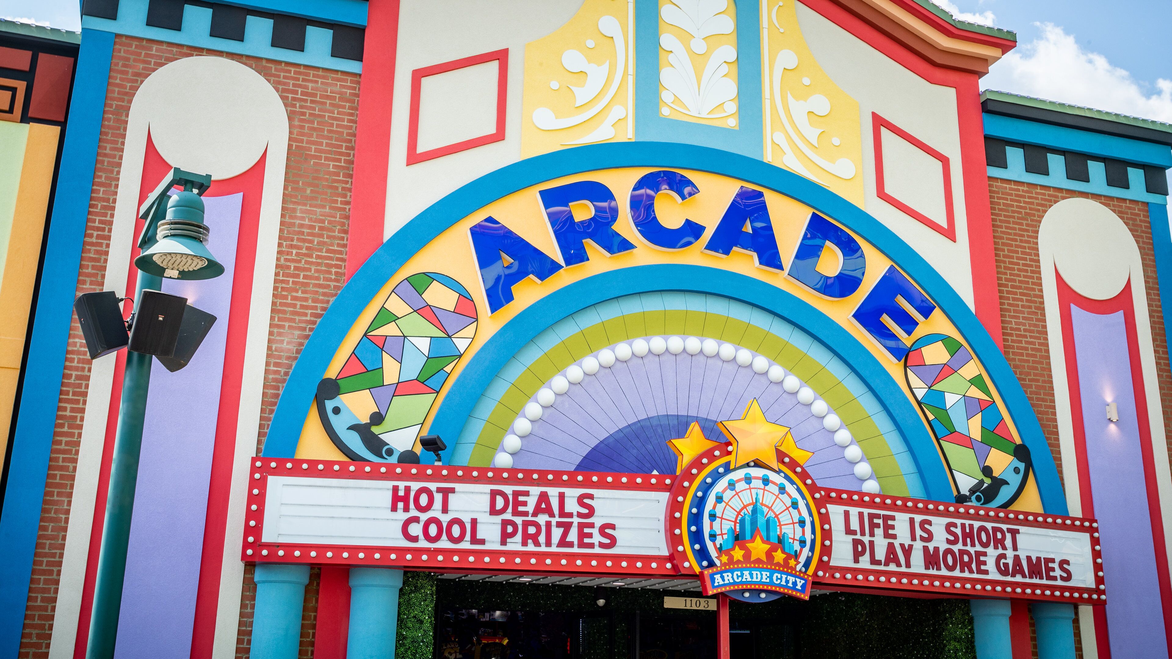 A colorful arcade building with a sign that reads "Arcade City" and "Life is short, play more games."
