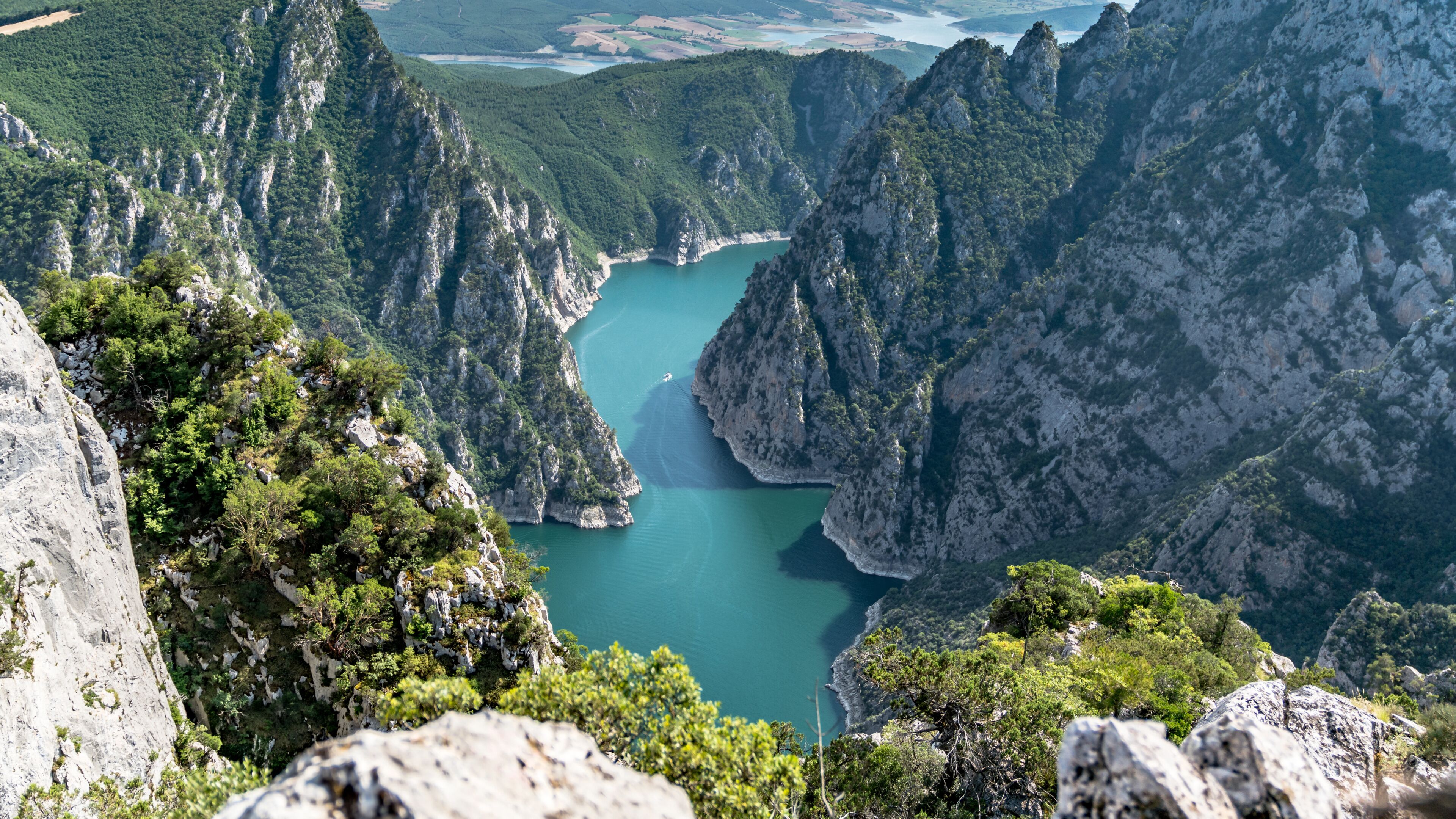 A mountainous landscape with a turquoise lake surrounded by steep cliffs and dense greenery.