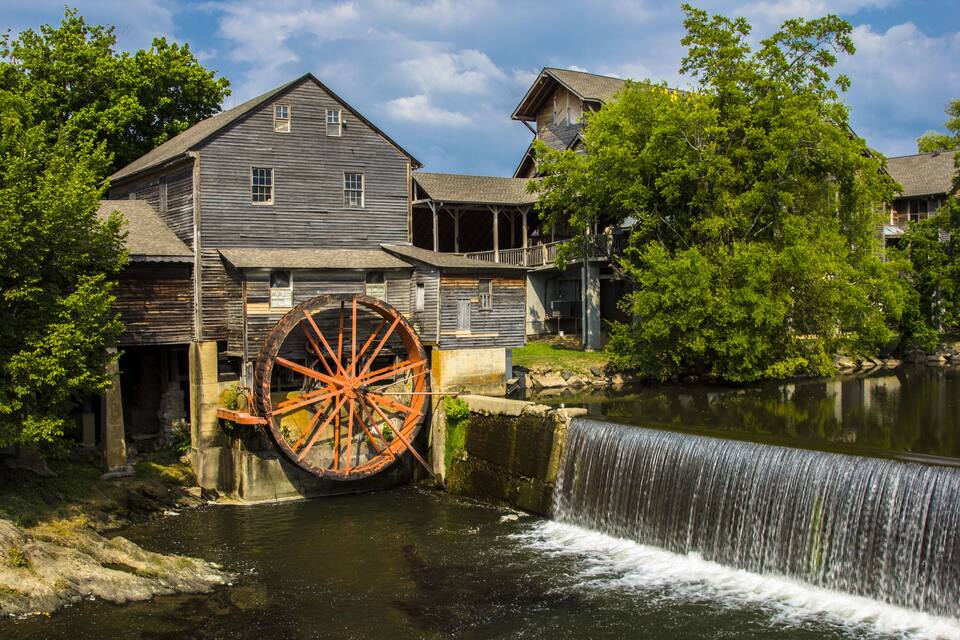 A historic water wheel and mill buildings by a river.