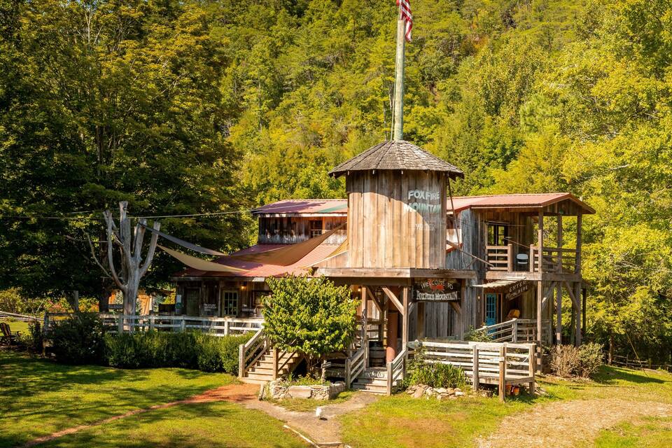 A wooden cabin with a flagpole, surrounded by lush green trees.
