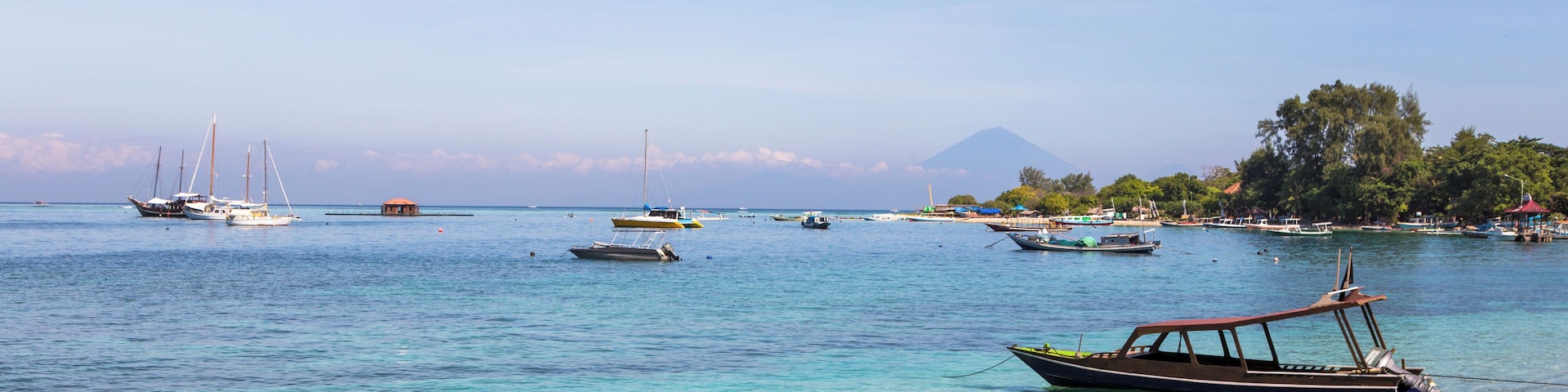 A coastal scene with boats anchored near the shore, a sandy beach, and a mountain in the background.