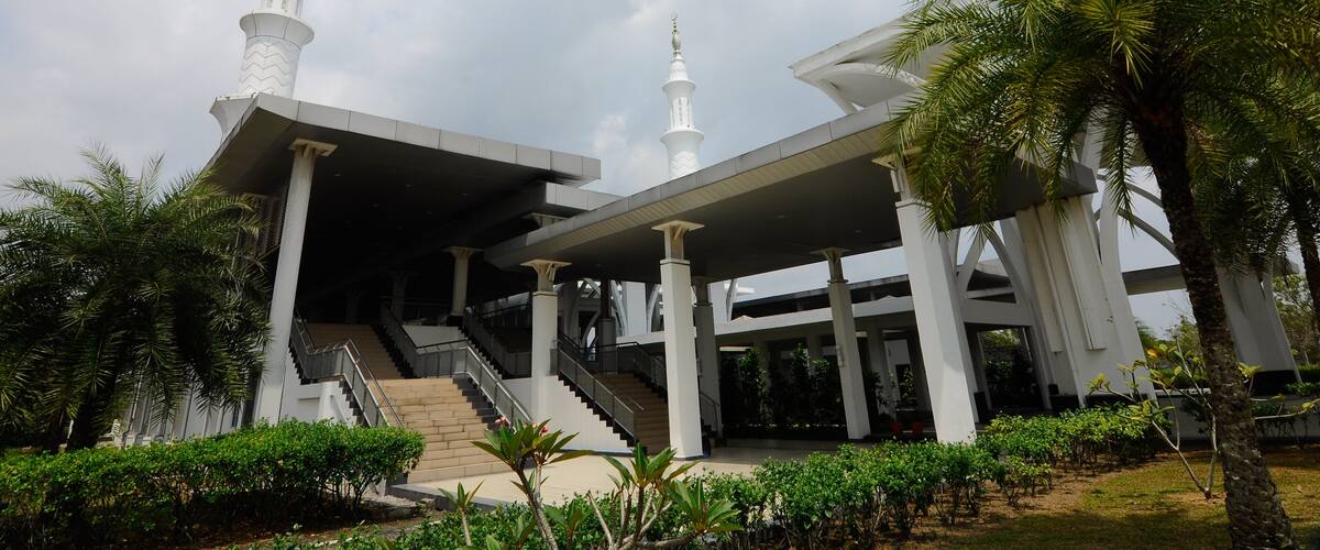 A modern building with two white minarets, a covered entrance, and a staircase leading up to the entrance.