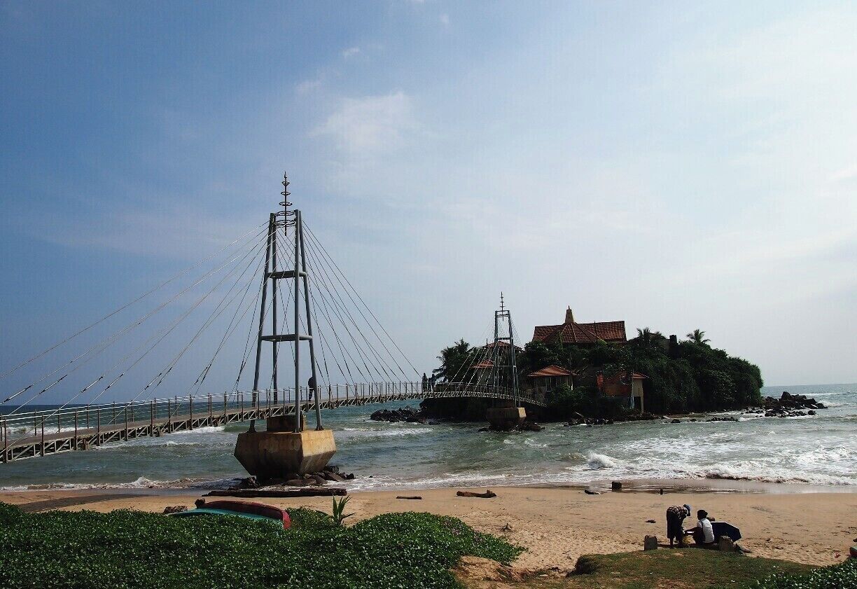 A coastal bridge, beach, and a small island with buildings.