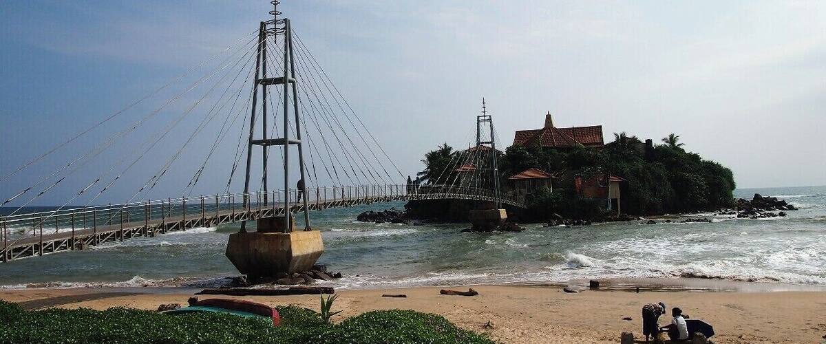 A coastal bridge, beach, and a small island with buildings.