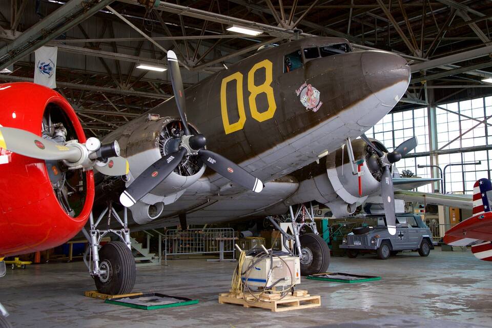 Una aeronave militar antigua con el número 08 en su fuselaje, exhibida en un hangar junto a otras aeronaves y equipo.