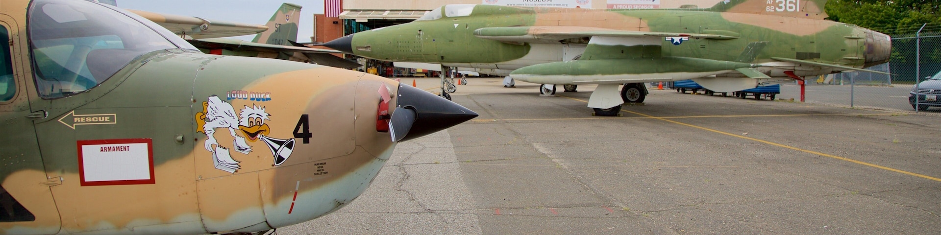 Aeronave militar estacionada em um aeródromo, com um edifício identificado como 'American Airpower Museum' ao fundo.