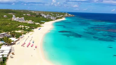 A coastal resort with a white sandy beach, turquoise waters, and a backdrop of lush greenery and buildings.