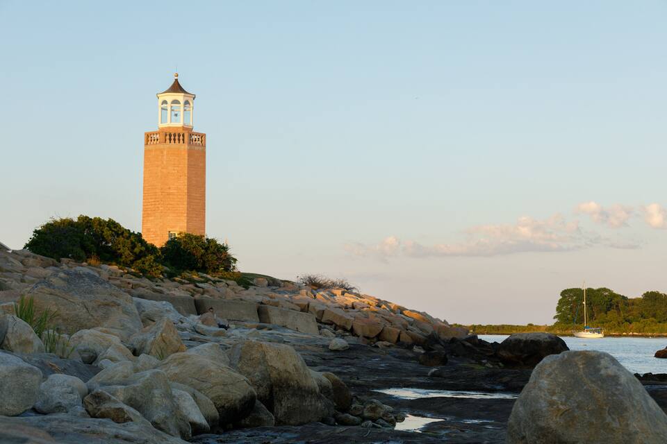 A lighthouse on a rocky shore with a boat in the water.