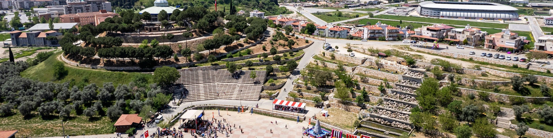 Una amplia plaza abierta con una fuente, rodeada de edificios y un estadio.