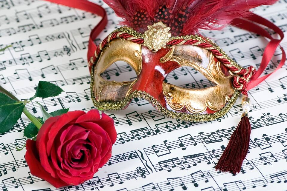 Un masque doré orné de motifs rouges et dorés, une rose rouge et une partition musicale.