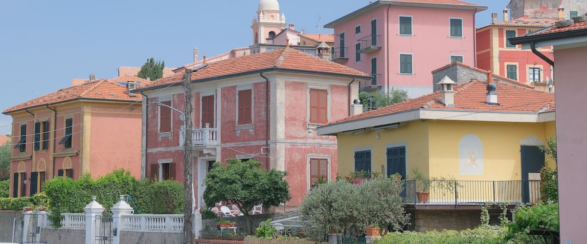 A row of colorful buildings with red-tiled roofs and balconies, surrounded by greenery.