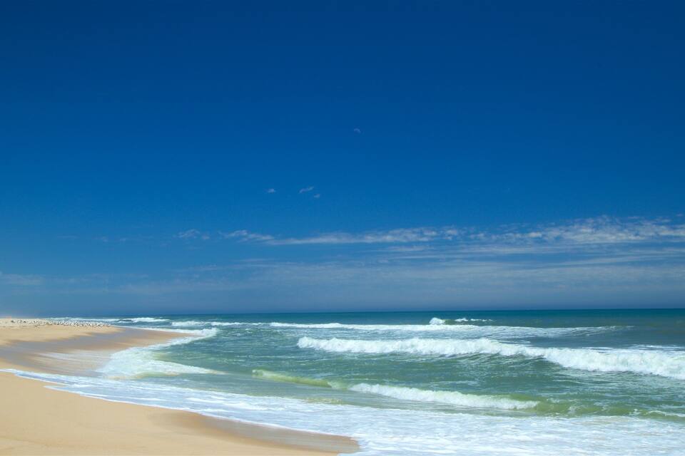 Ein Strand mit Wellen, blauem Himmel und einem sichelförmigen Mond.