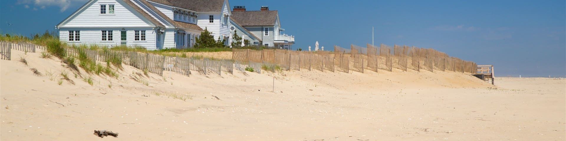 A white house on a sandy beach with a wooden fence.
