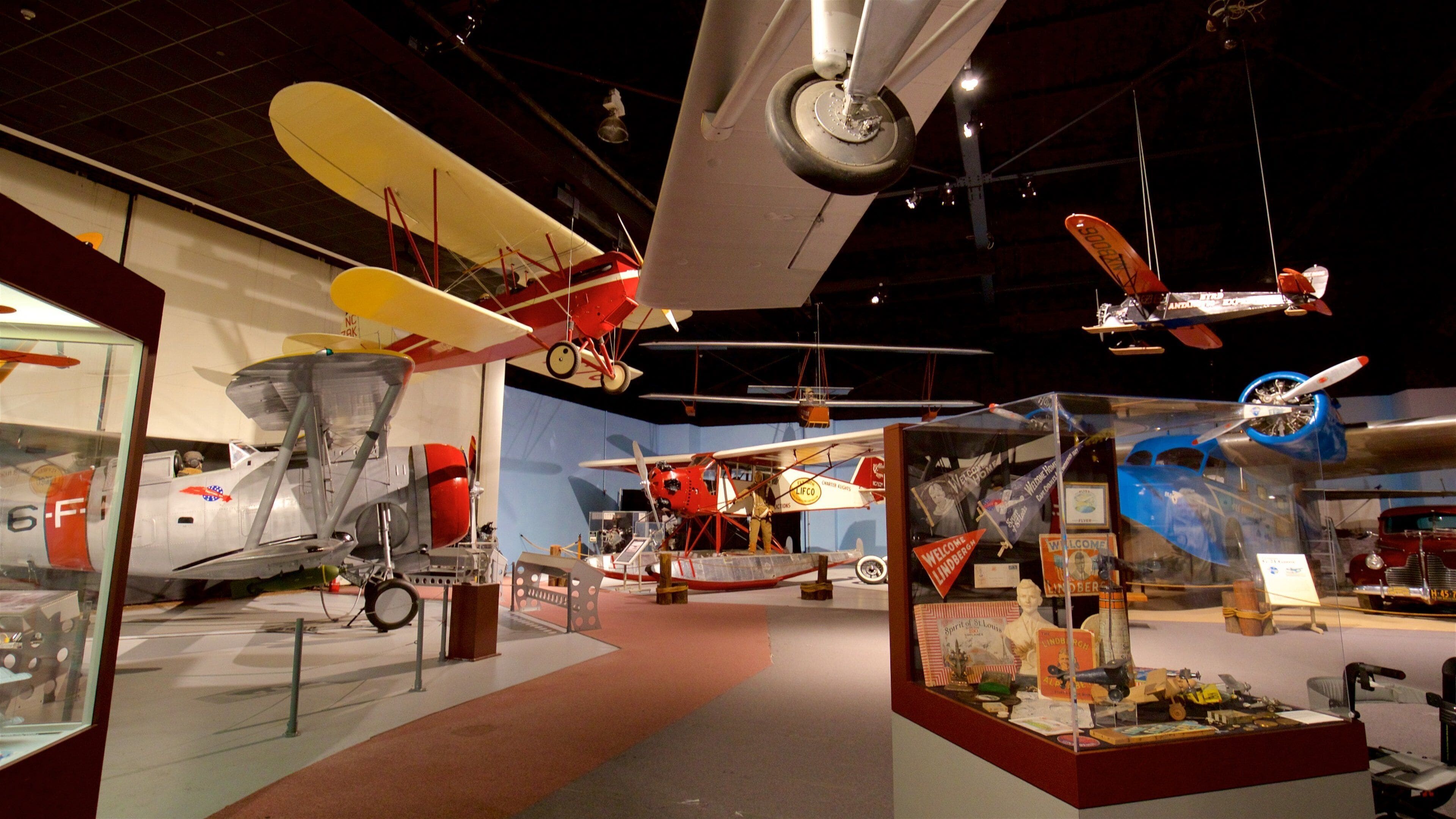 A museum exhibit with various aircraft models, including biplanes and a vintage car.