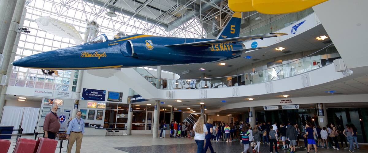A blue and yellow airplane with 'US NAVY' and 'Blue Angels' written on it, suspended in a building with a glass ceiling.