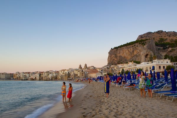 Une plage animée, avec des parasols bleus et des bâtiments historiques.