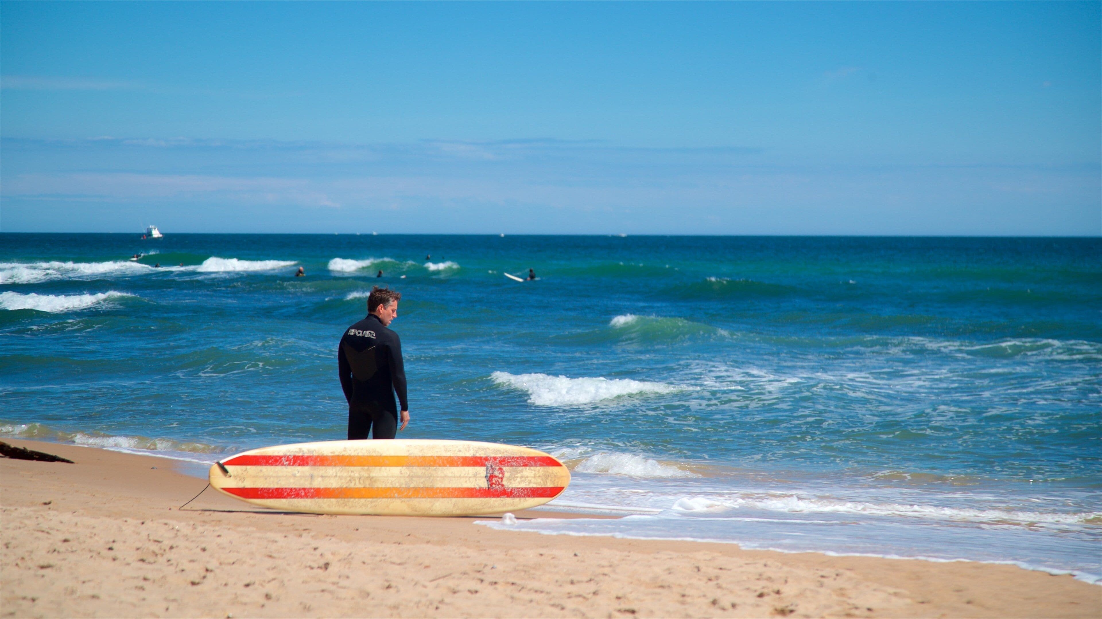 Una playa con un surfista de pie sobre la arena, sosteniendo una tabla de surf.