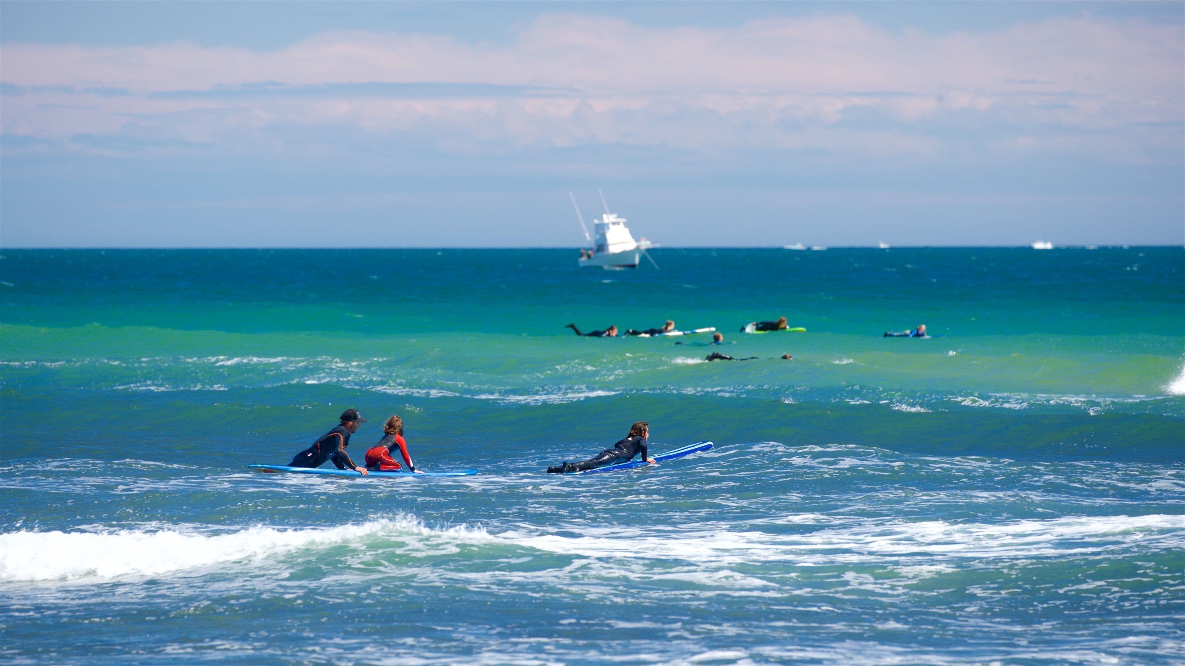 Des surfeurs sur l’océan, avec un bateau visible au loin.