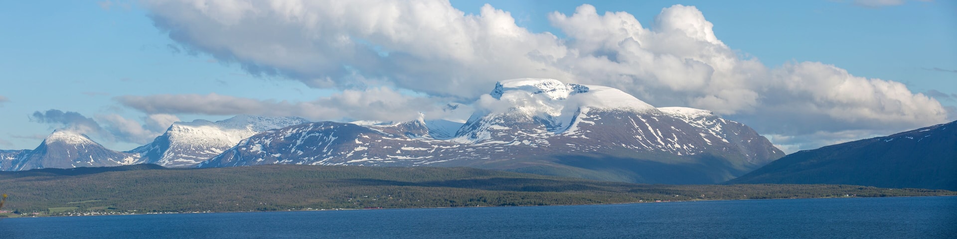 A mountain range with snow-capped peaks and a body of water in the foreground.