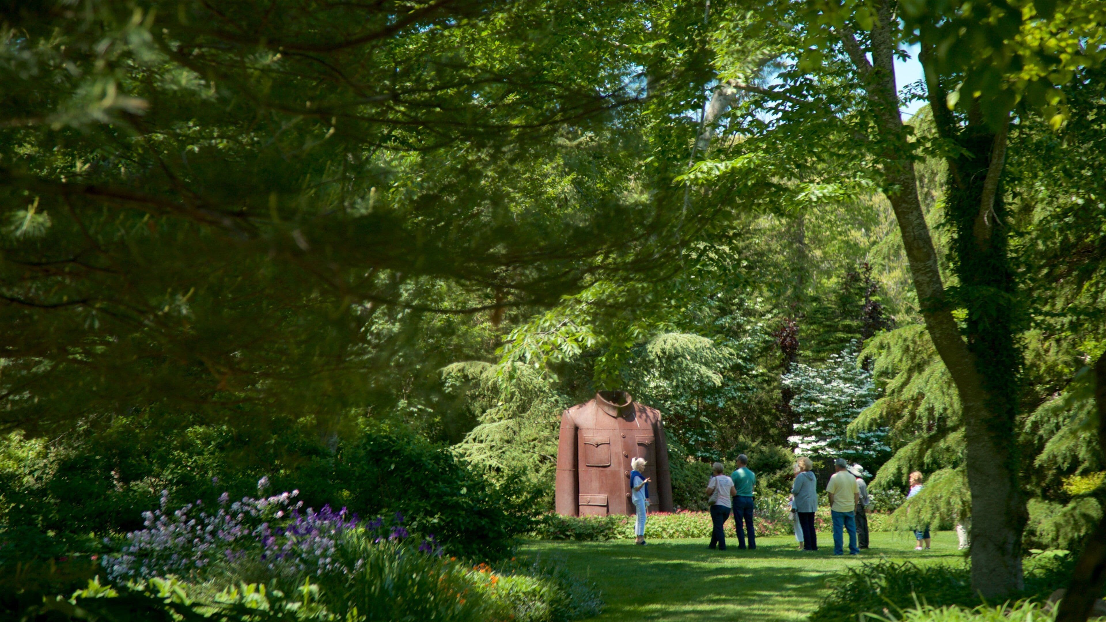 A garden with a statue, lush greenery, and a group of people walking.