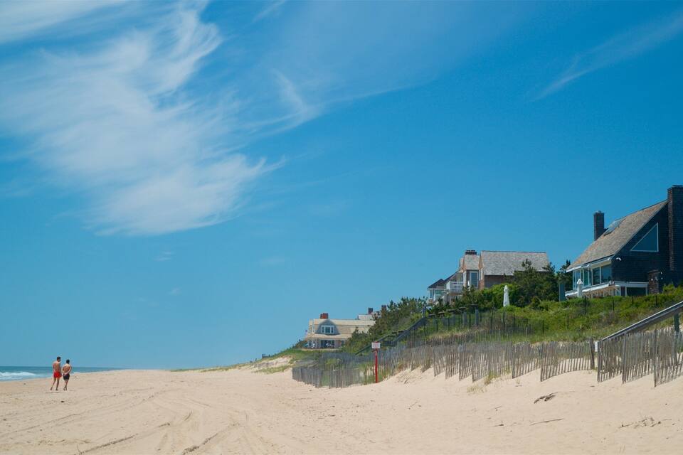 A beach with a wooden fence, a house, and two people walking.