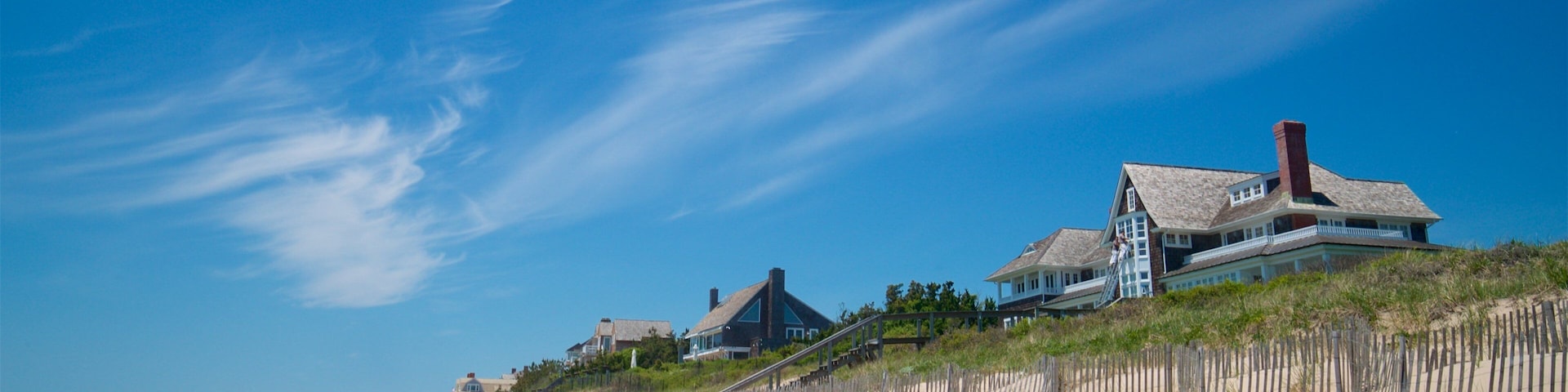A sandy beach with wooden fences and houses on a dune.