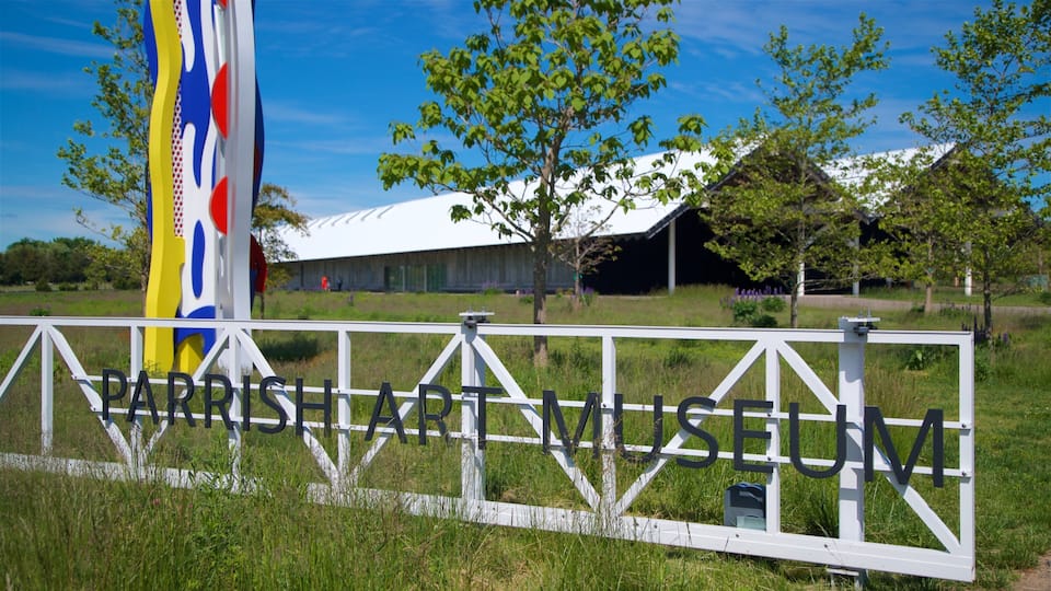 A sign for the Parrish Art Museum surrounded by a white fence and greenery.