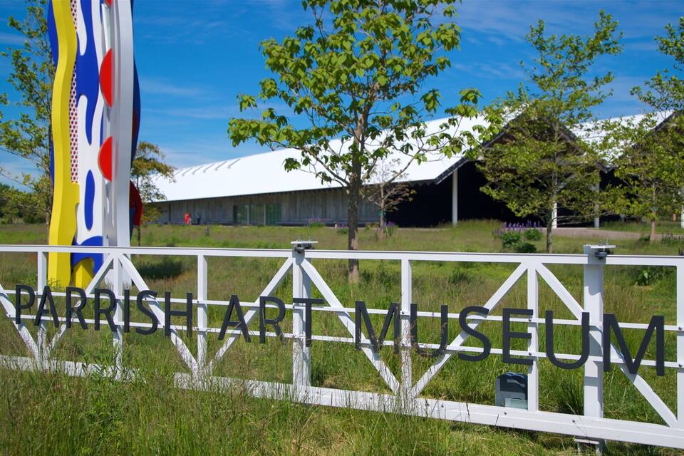 A sign for the Parrish Art Museum surrounded by a white fence and greenery.