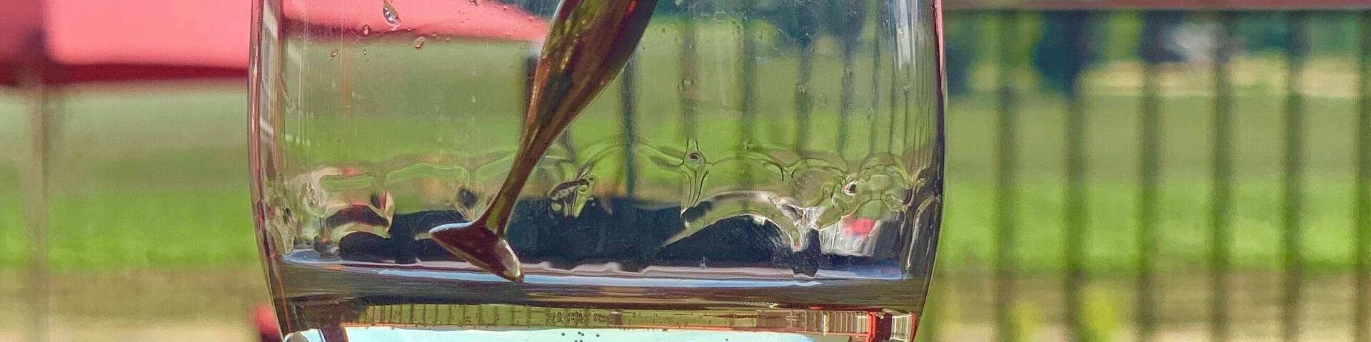 Una copa de vino blanco con un asa roja, con un cielo azul claro y montañas lejanas al fondo.