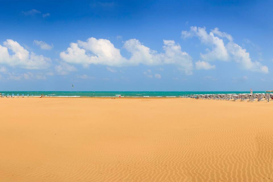 A wide sandy beach with a clear blue sky and scattered clouds.