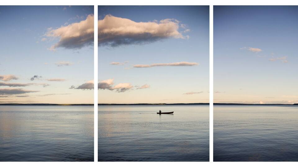 A calm lake with a small boat, surrounded by trees and a clear sky with clouds.