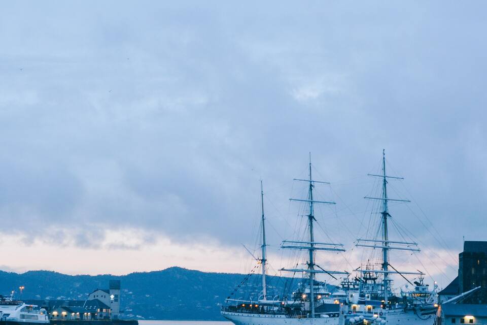Un puerto con varios barcos de vela y un paisaje montañoso al fondo.
