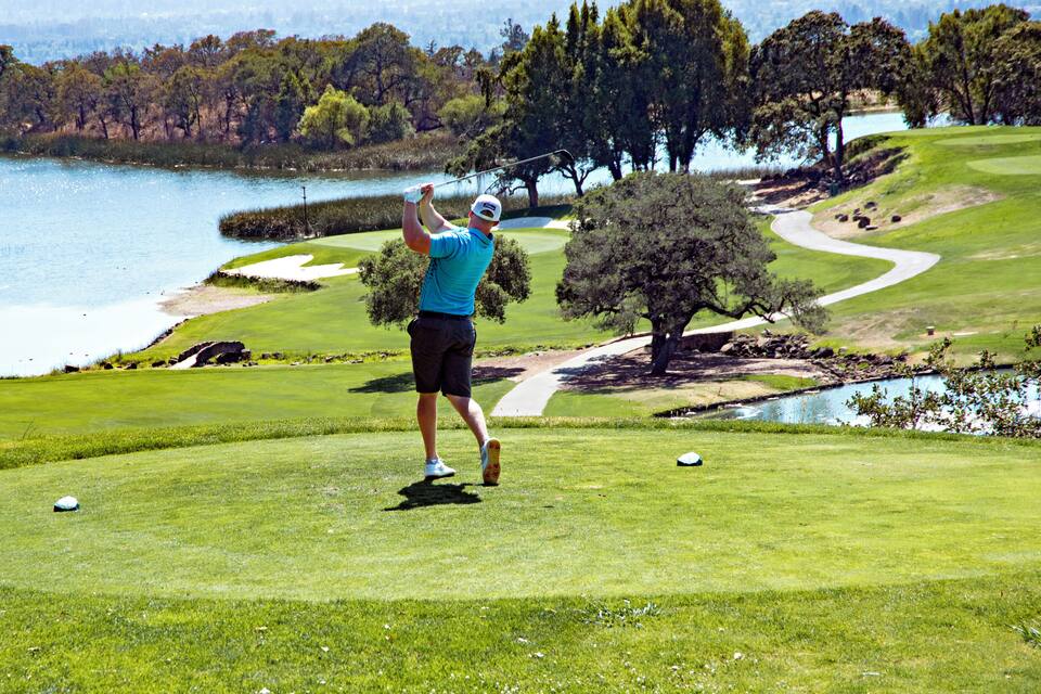 A golfer on a golf course with a lake and trees in the background.