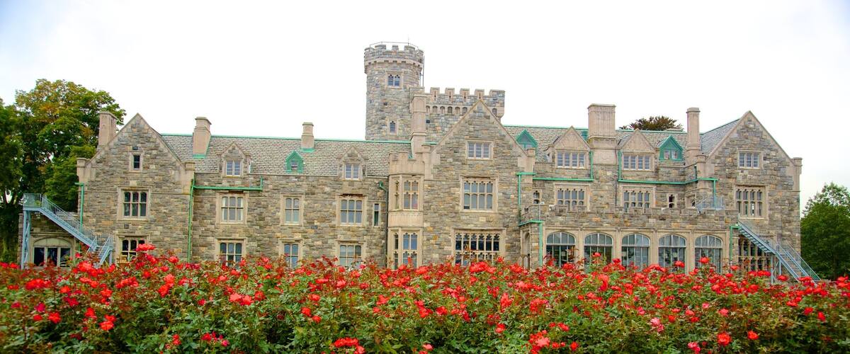 A large stone building with a turret and multiple windows, surrounded by a garden of red roses.