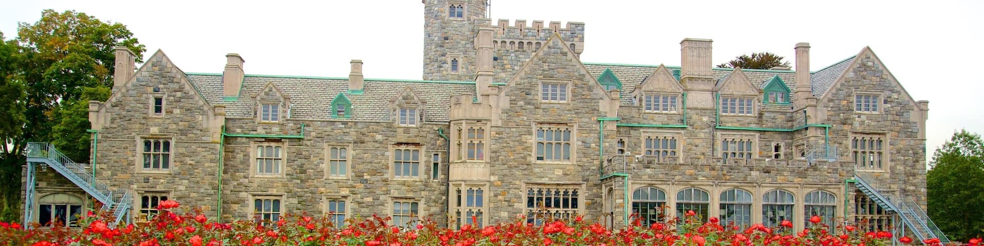 A large stone building with a turret and multiple windows, surrounded by a garden of red roses.