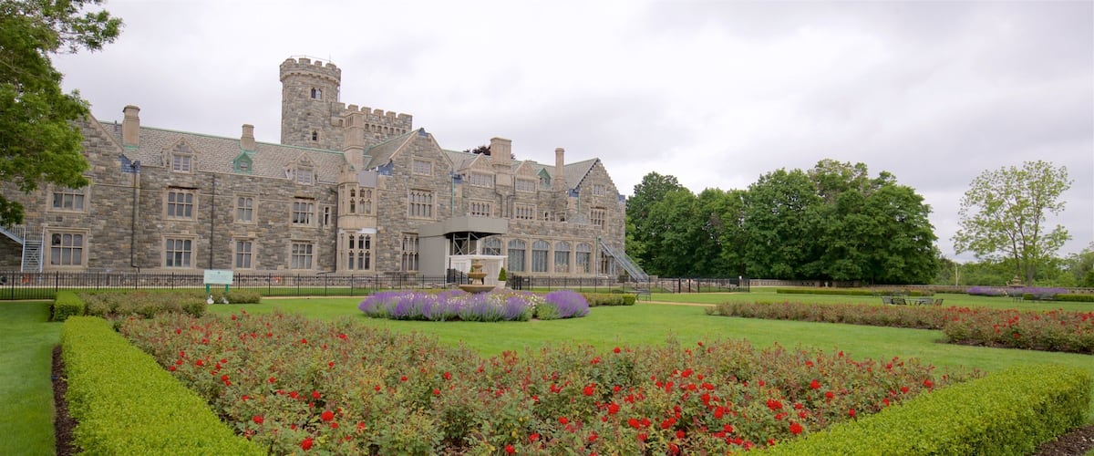 A large stone building with a tower, surrounded by well-manicured gardens and trees.