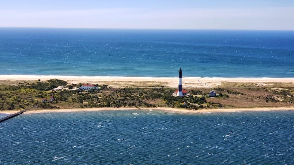 A lighthouse on a small island with a beach and ocean.