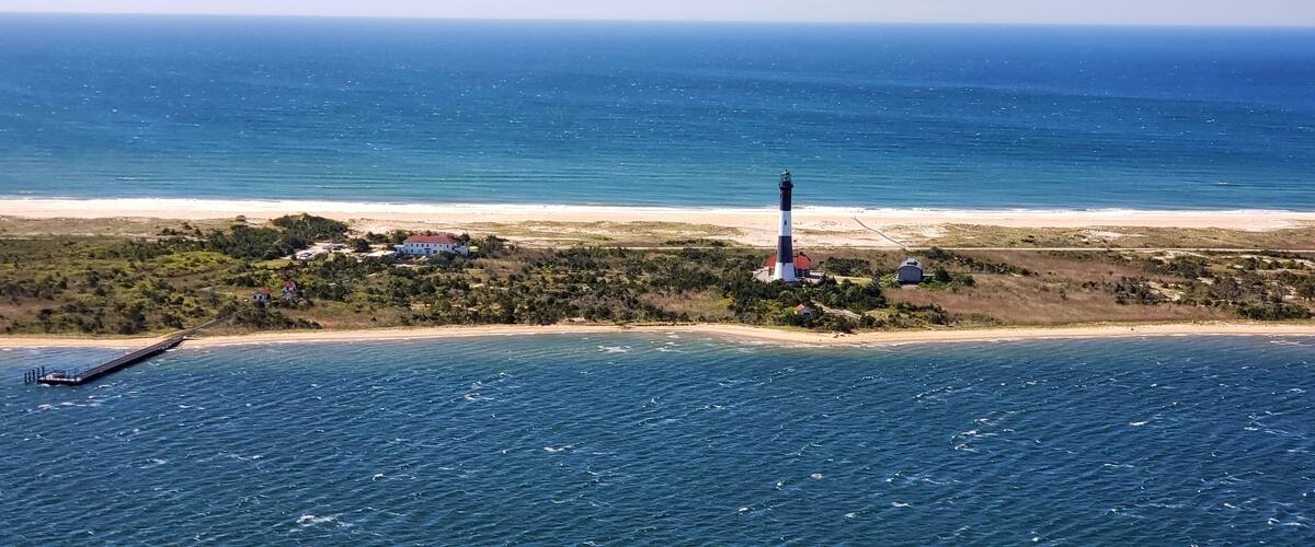 A lighthouse on a small island with a beach and ocean.