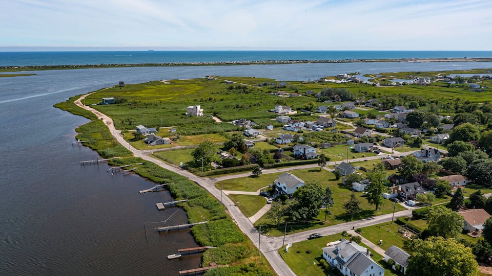 An aerial view of a coastal residential area with houses, a marina, and a large body of water.