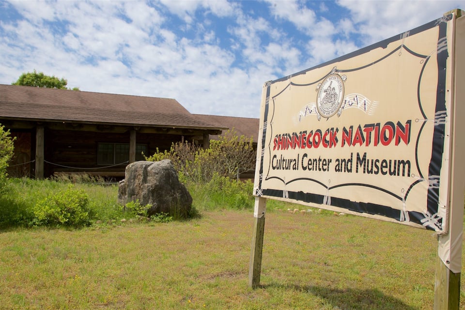 A sign for the Shinnecock Nation Cultural Center and Museum with a wooden building in the background.