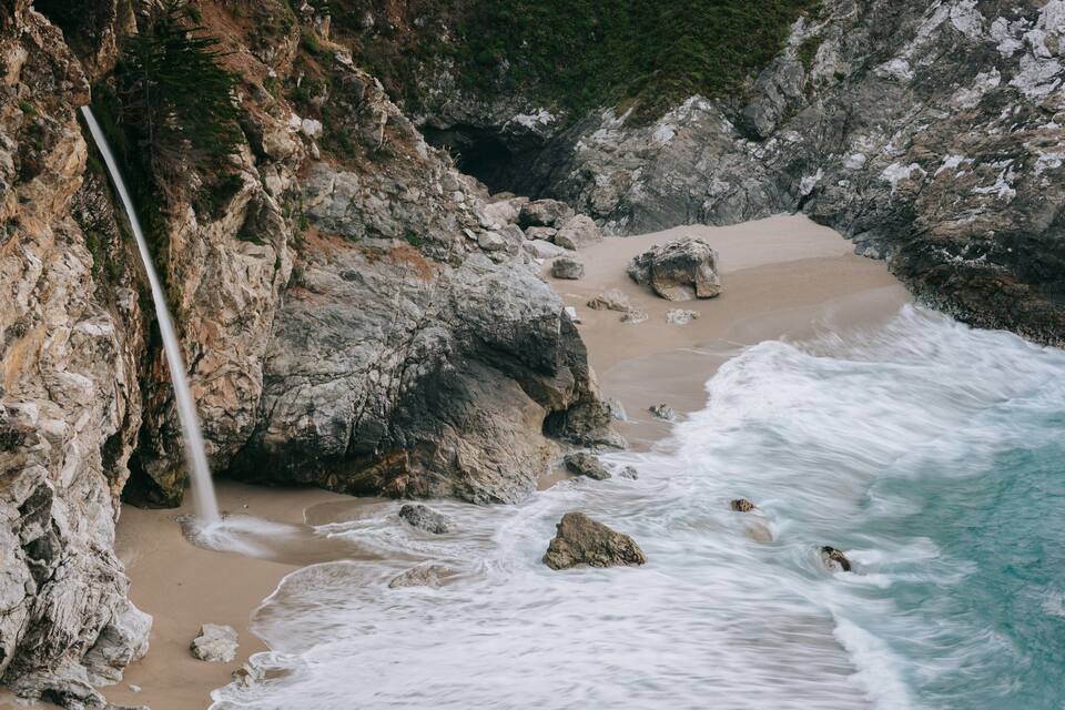 Eine Küstenlandschaft mit einem Wasserfall, steinigen Klippen und brechenden Wellen.