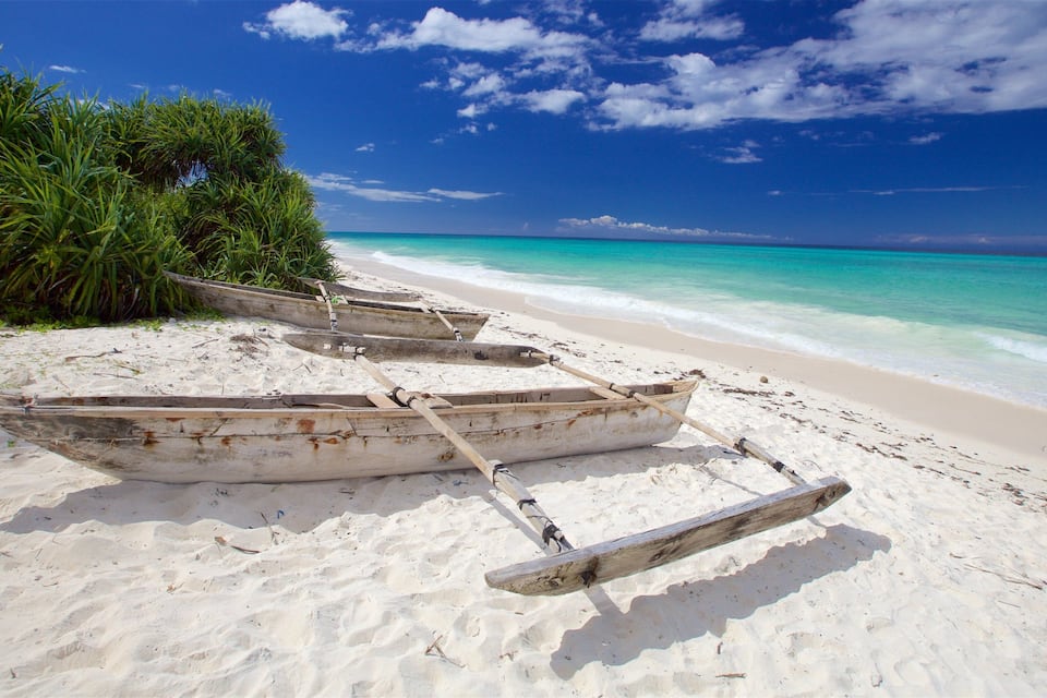 Ein sandiger Strand mit drei hölzernen Booten und üppiger, grüner Vegetation.