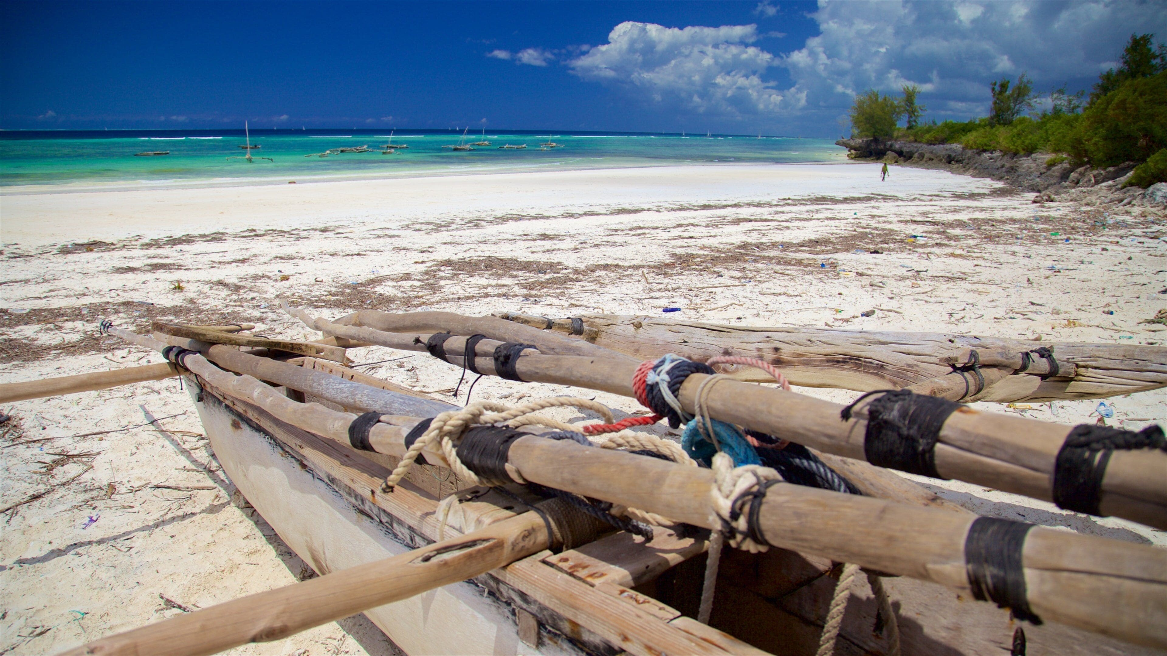 A beach with wooden boats tied to a wooden structure, a clear blue sky, and turquoise water.