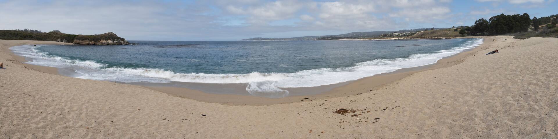A sandy beach with gentle waves, a clear sky, and distant hills.