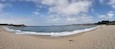 A sandy beach with gentle waves, a clear sky, and distant hills.