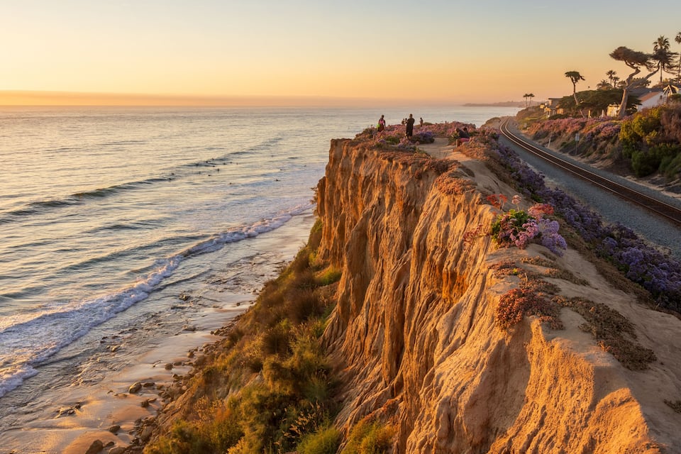 A coastal landscape with a cliff, beach, and a railway track.