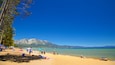 Une plage ensoleillée où des gens se prélassent au soleil, un bateau sur l’eau et des montagnes en arrière-plan.