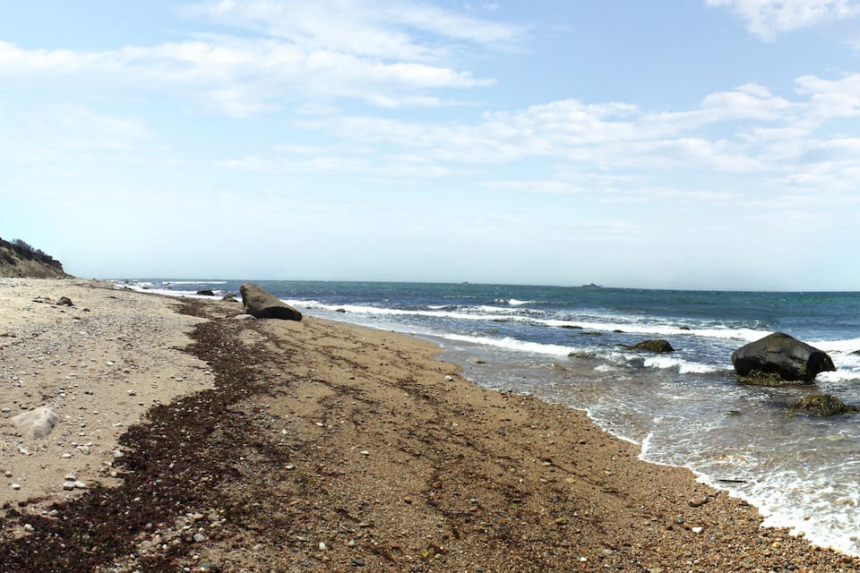 A rocky beach with waves crashing onto the shore and a cliff in the background.