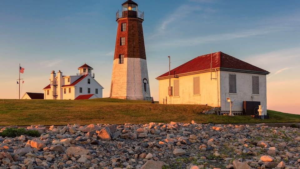 A lighthouse, a white building with a red roof, and a rocky shoreline.