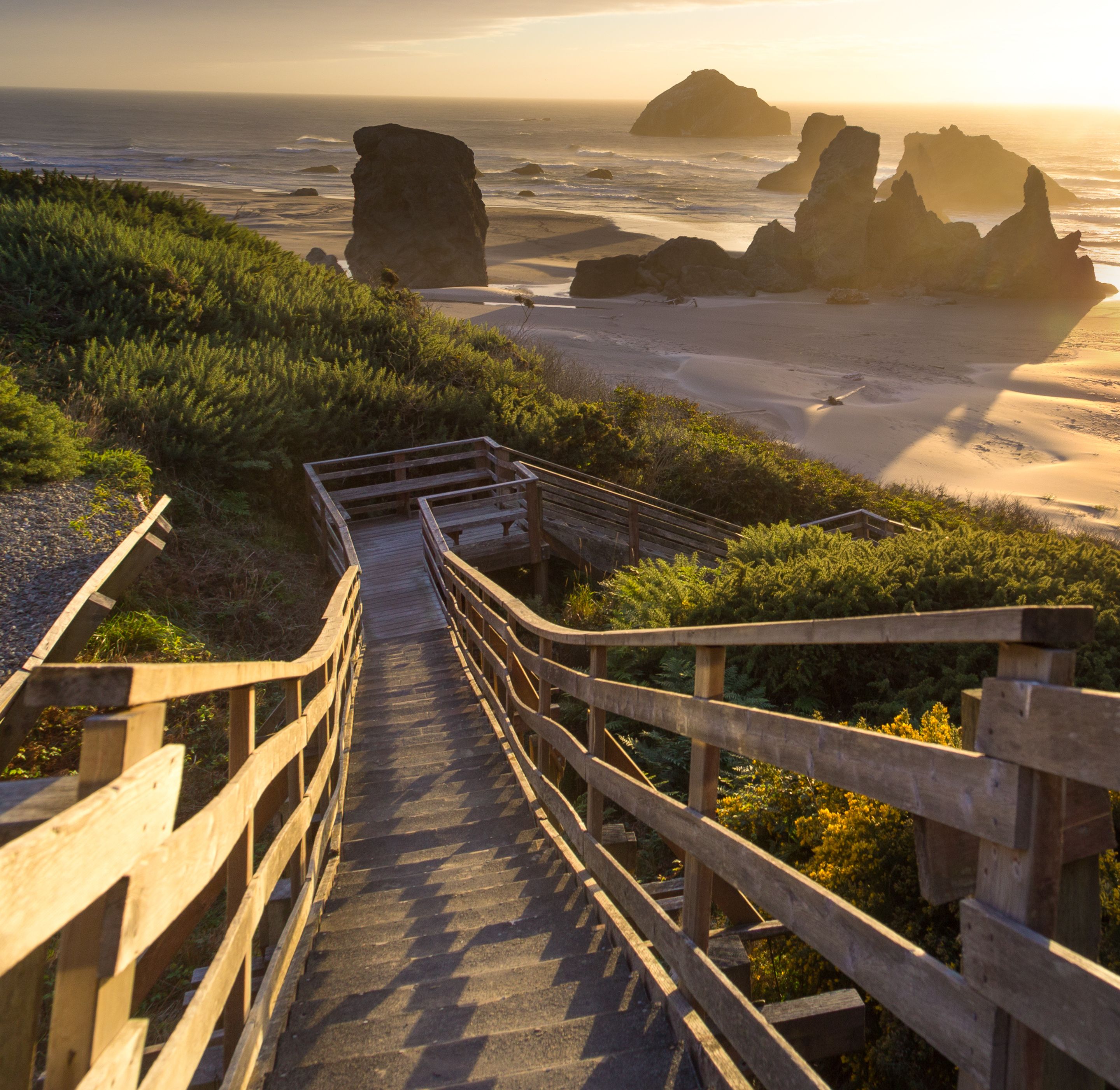 A wooden staircase leading to a beach with rocky formations in the background.